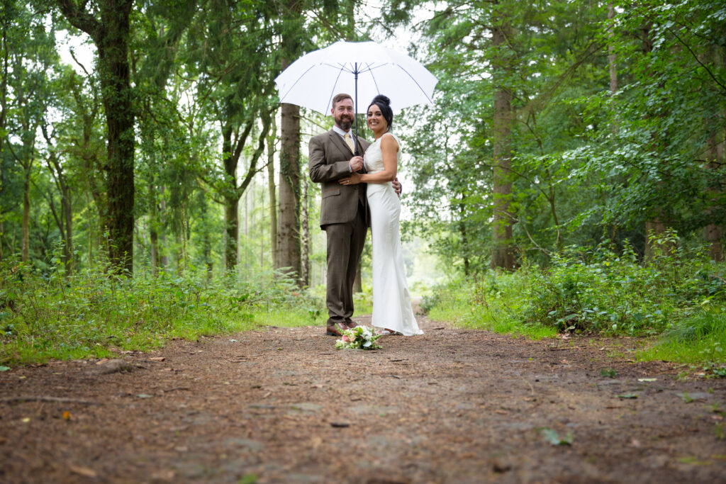 Couple in wedding attire in the rain in the Forest, Gloucestershire